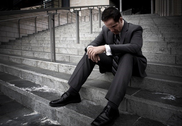 A distraught man sits on the steps of an office building.